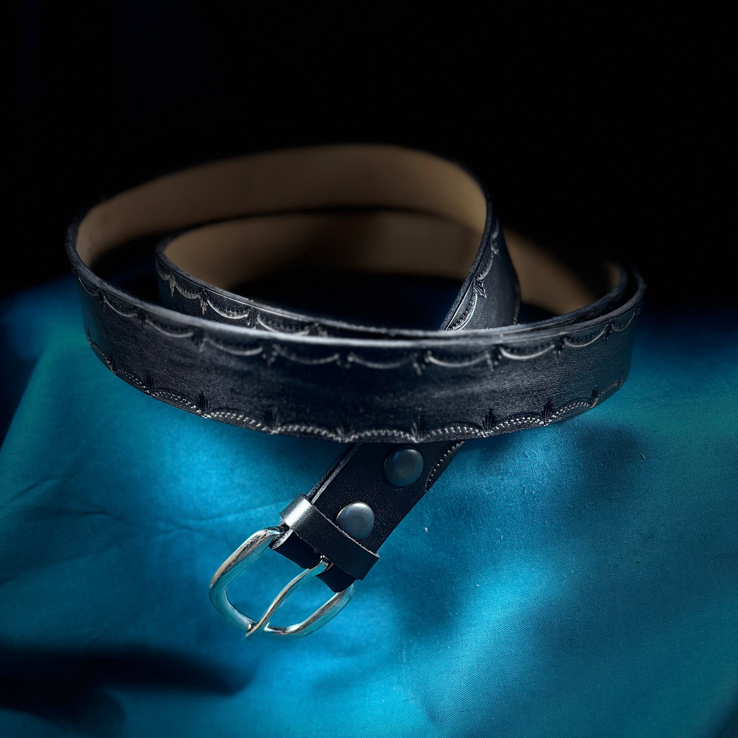 Black leather belt with silver buckle on a blue fabric background