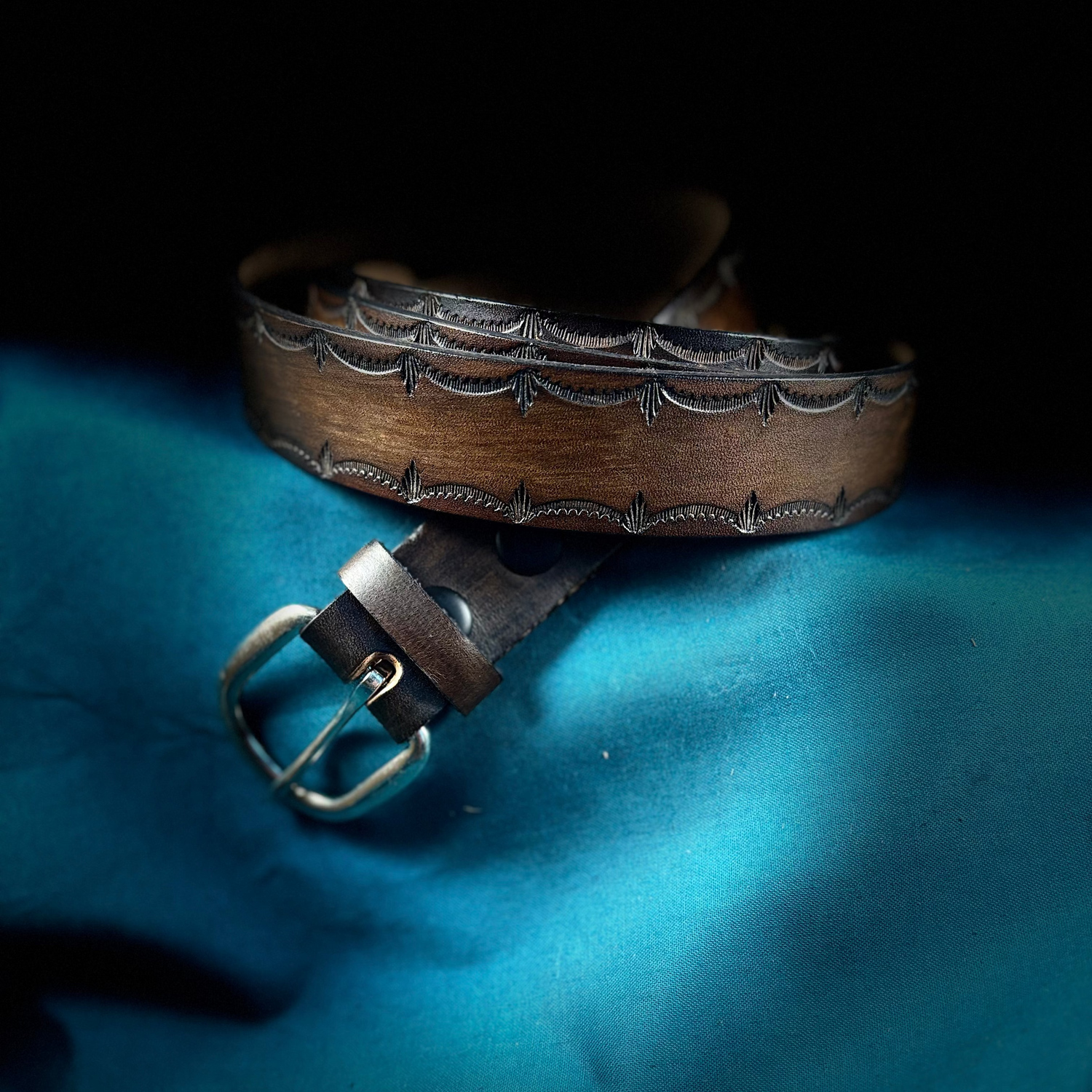 Brown leather belt with silver buckle on a blue fabric background