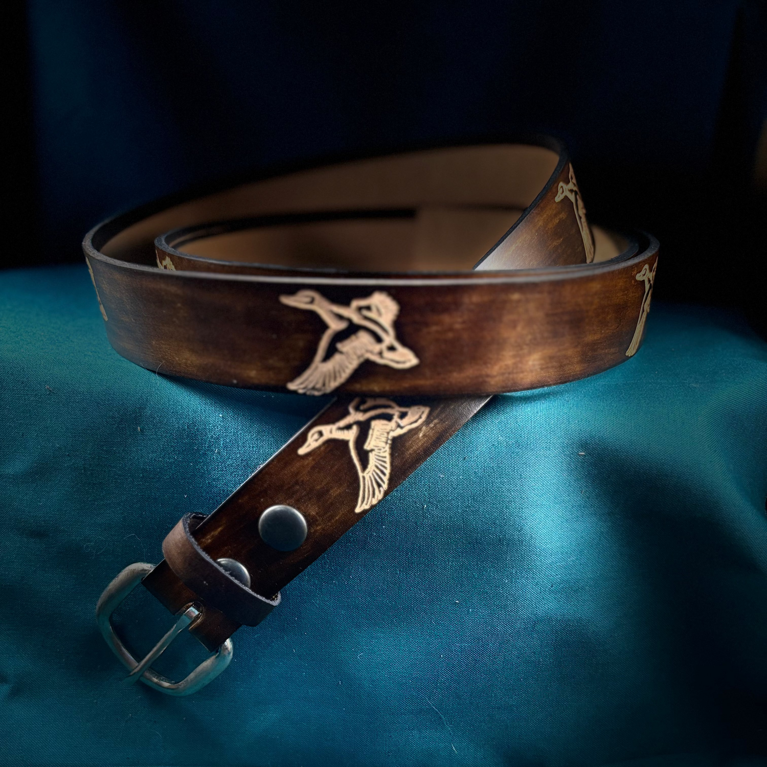 Brown leather belt with silver buckle and embossed design on a blue fabric background