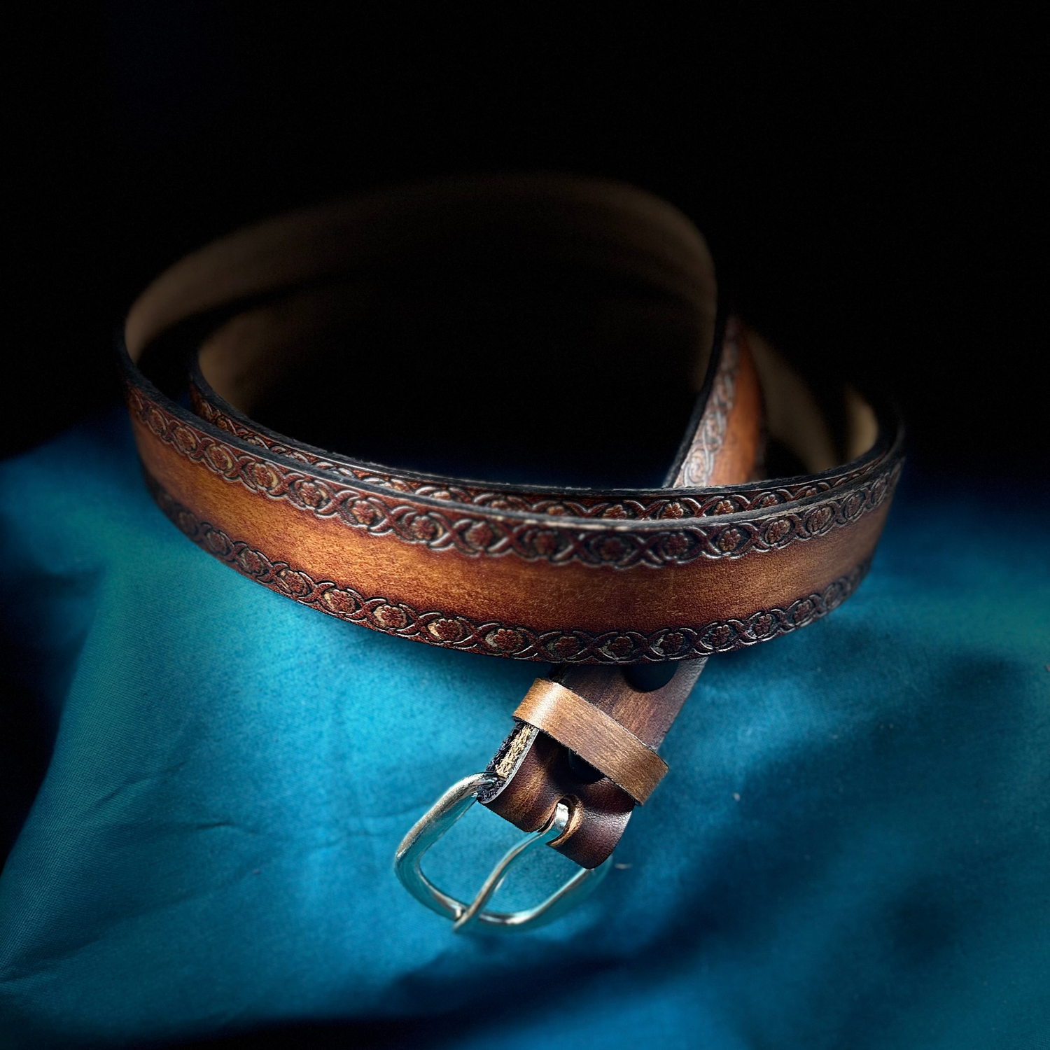 Brown leather belt with intricate design on a blue fabric background