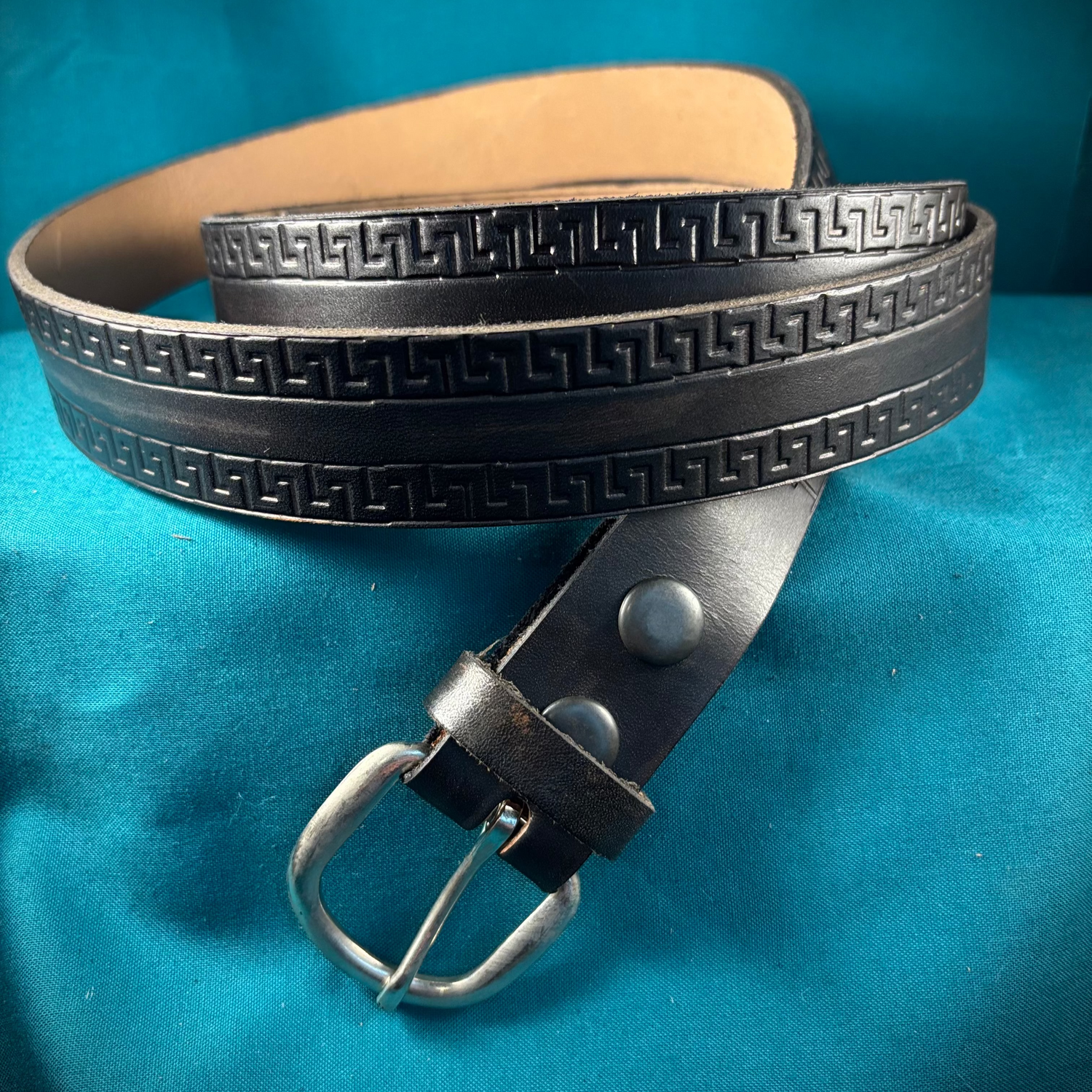 Black leather belt with metallic buckle on a blue background
