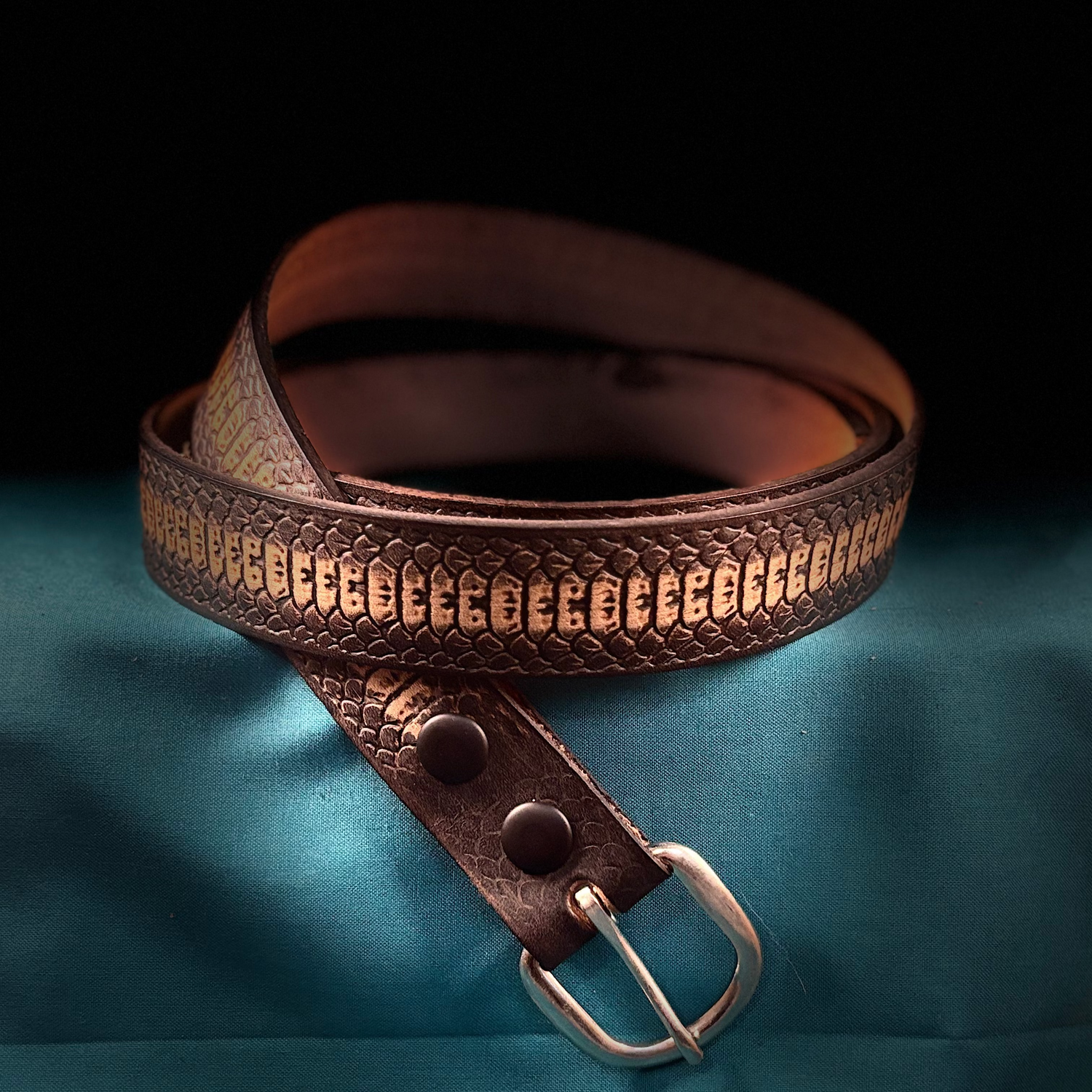 Mahogany Brown leather belt In Snakeskin pattern with metal buckle on a blue fabric background