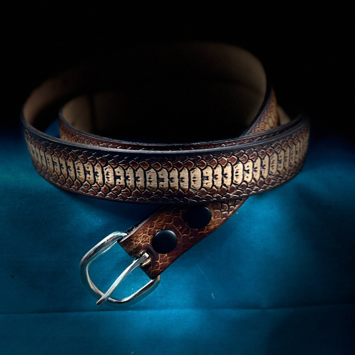 Brown leather snakeskin pattern belt with metallic buckle on a blue background