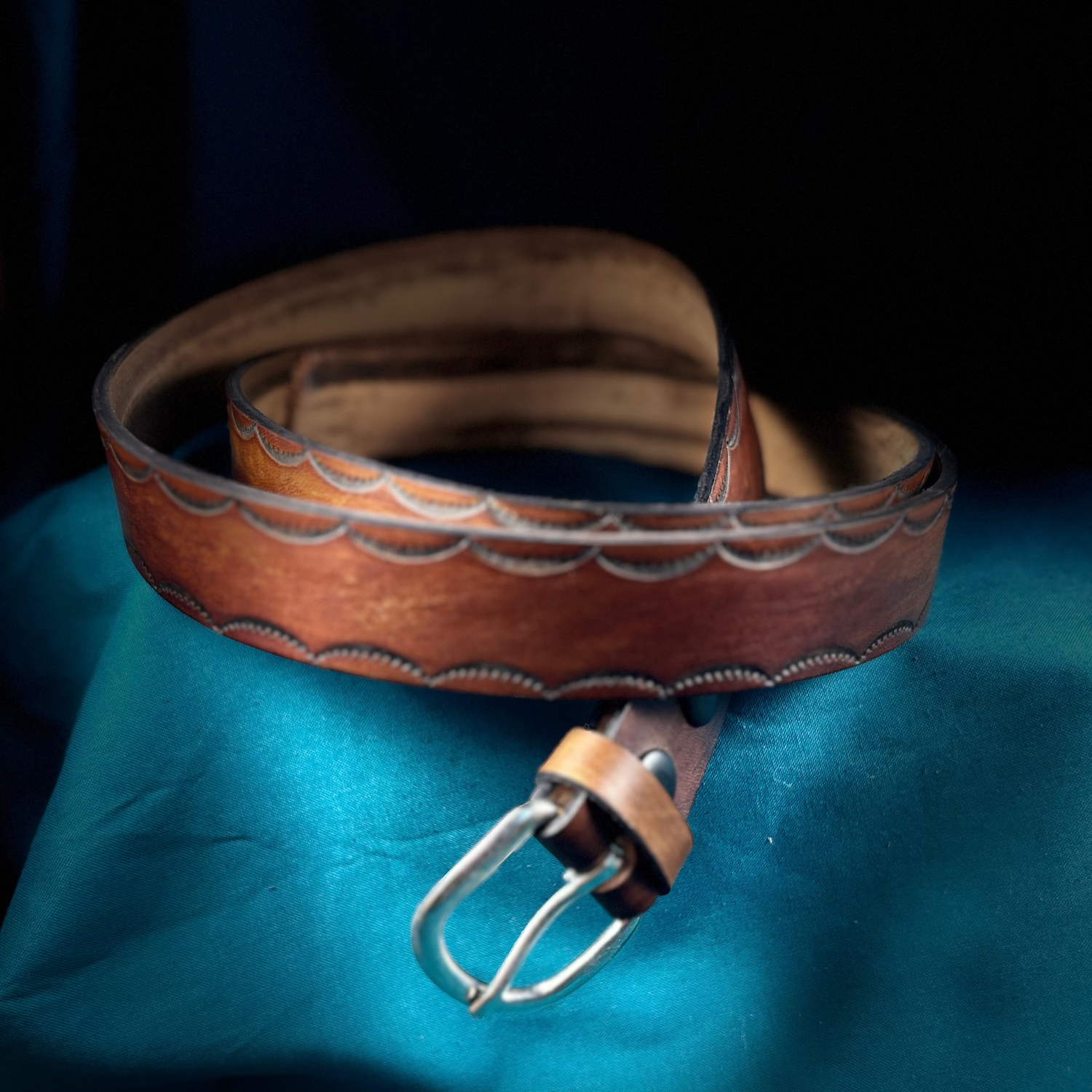 Brown leather belt with a silver buckle on a blue fabric background