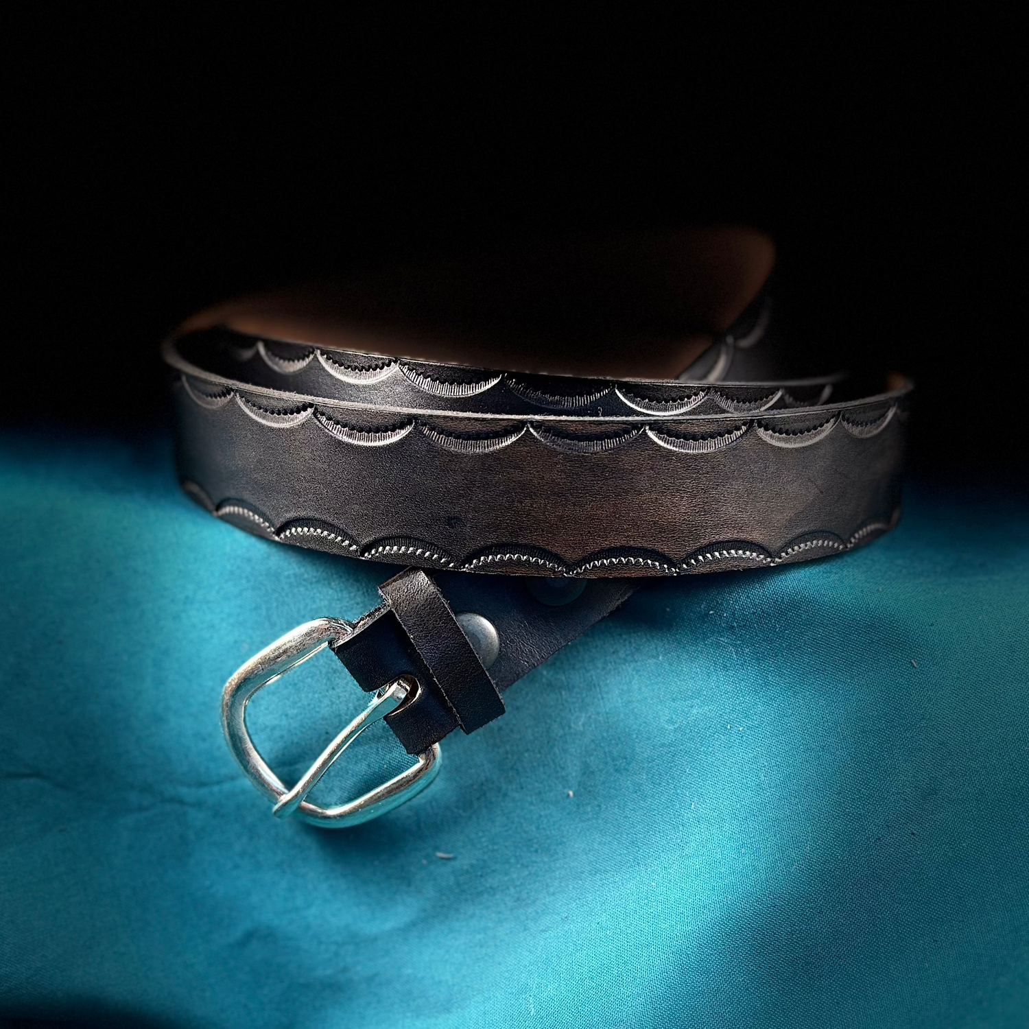 Brown leather belt with silver buckle on a blue fabric background