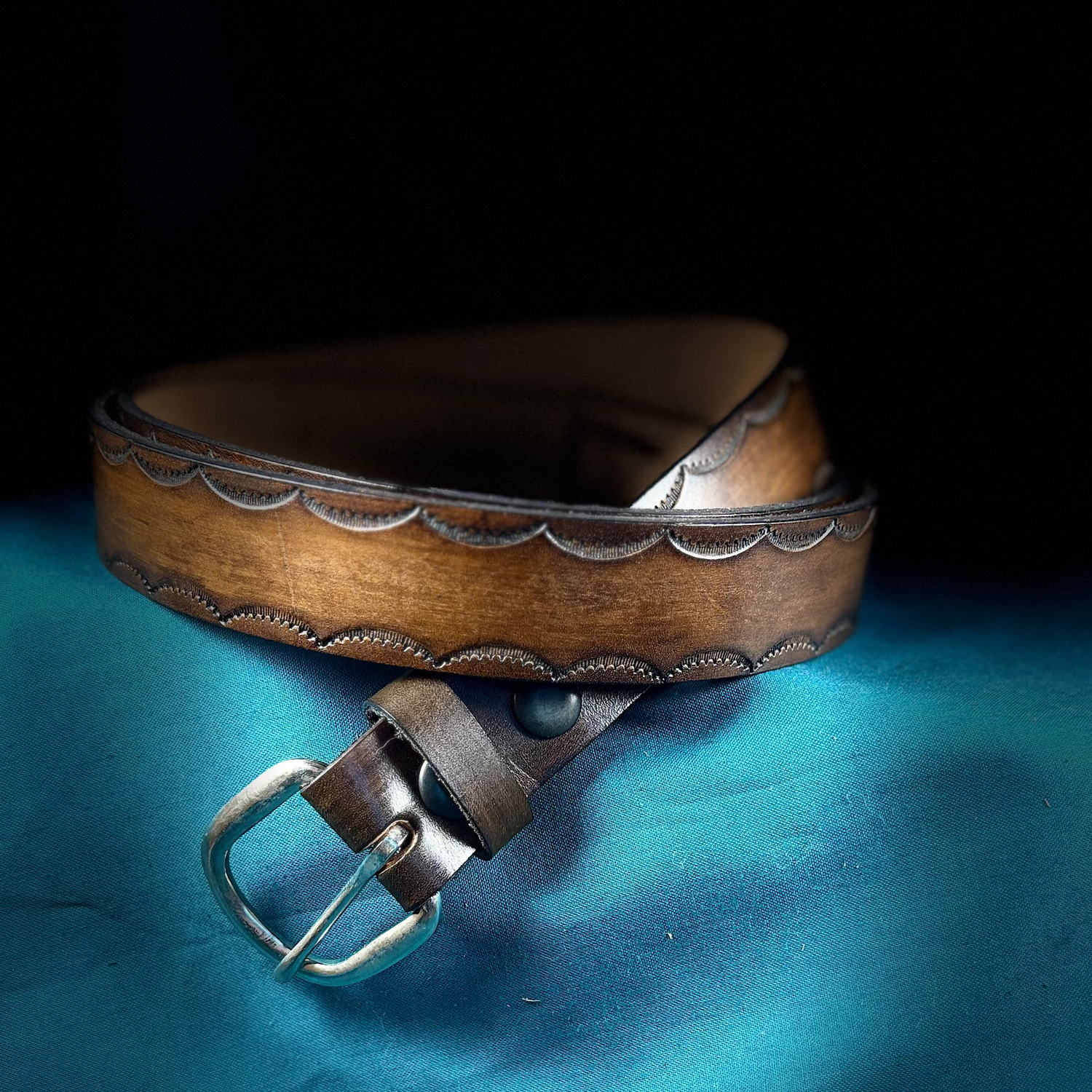 Brown leather belt with silver buckle on a blue fabric background