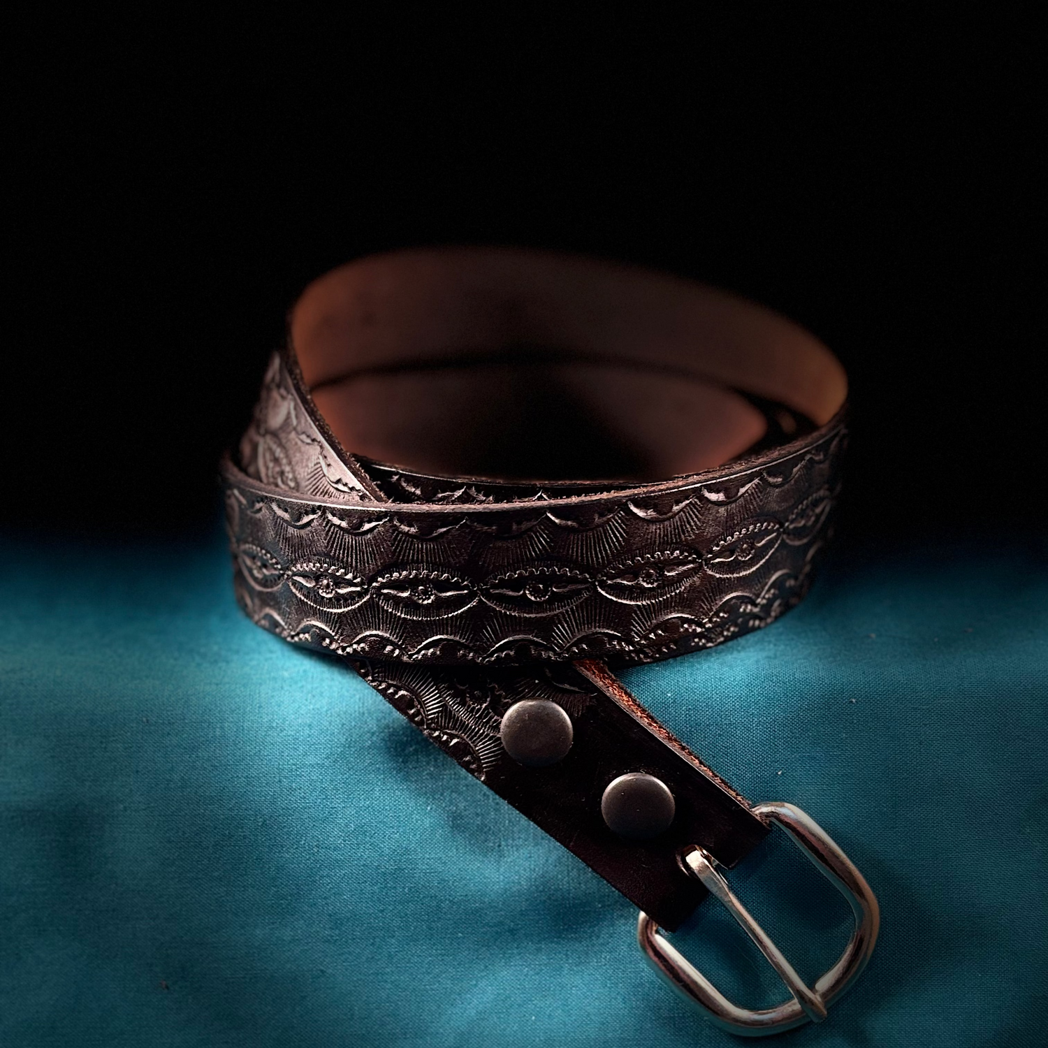 Brown leather belt with intricate design on a blue fabric background