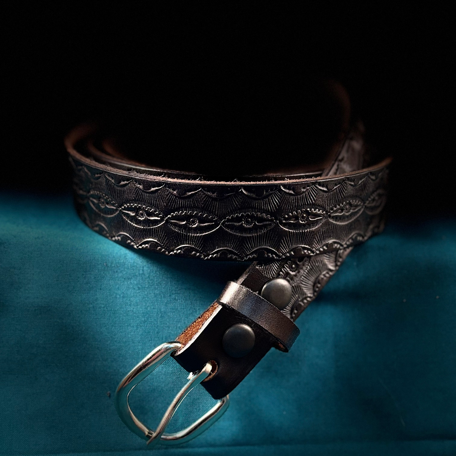 Brown leather belt with embossed design on a blue fabric background
