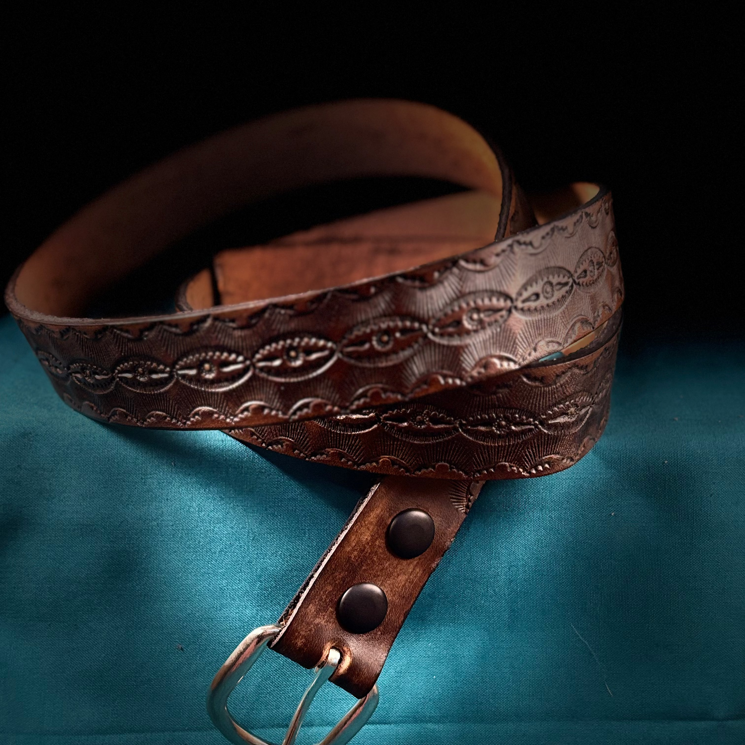 Brown leather belt with embossed design on a blue fabric background