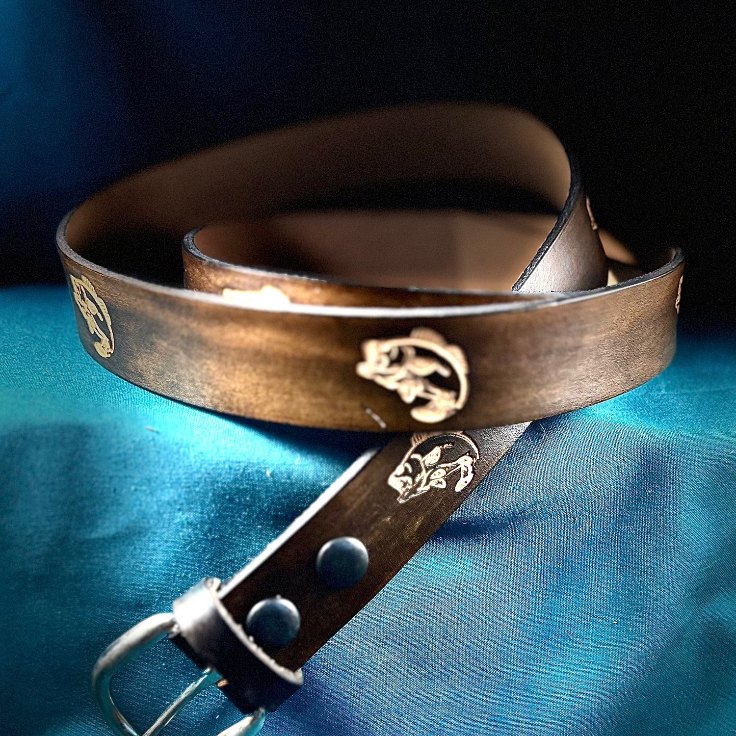 Brown leather belt with metal buckle on a blue fabric background