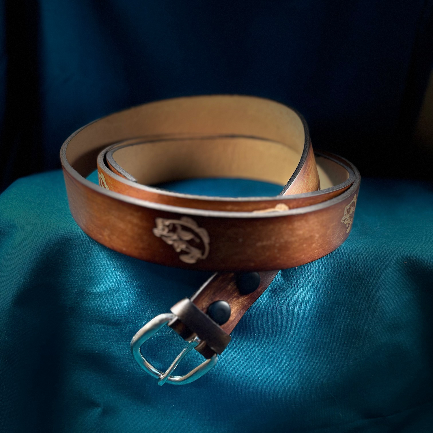 Brown leather belt with silver buckle on a blue fabric background