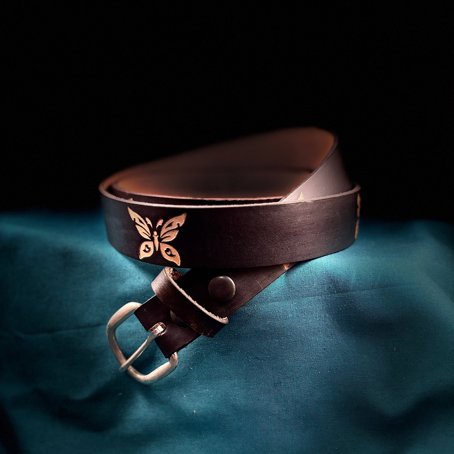 black leather belt with butterfly design buckle on a dark background