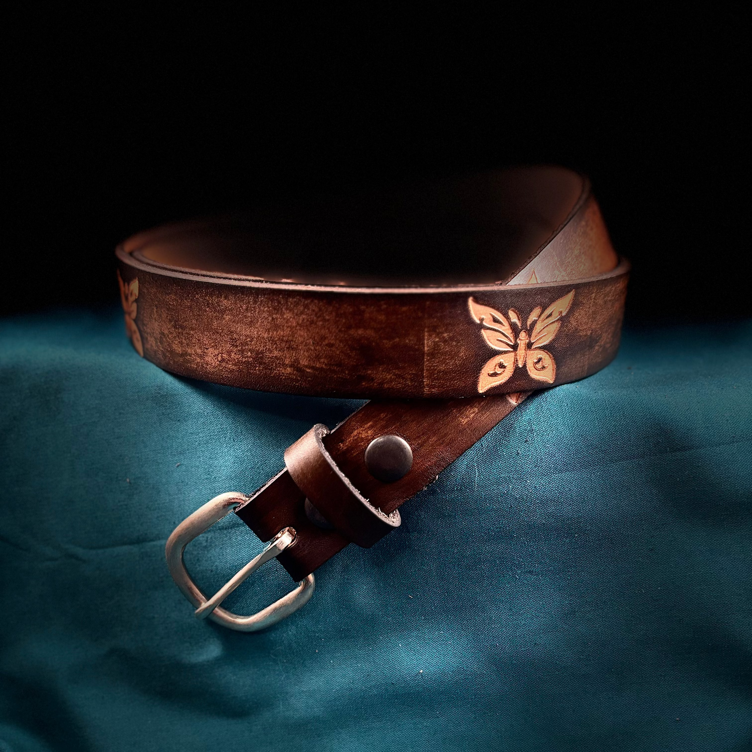 Brown leather belt with butterfly design on a blue fabric background
