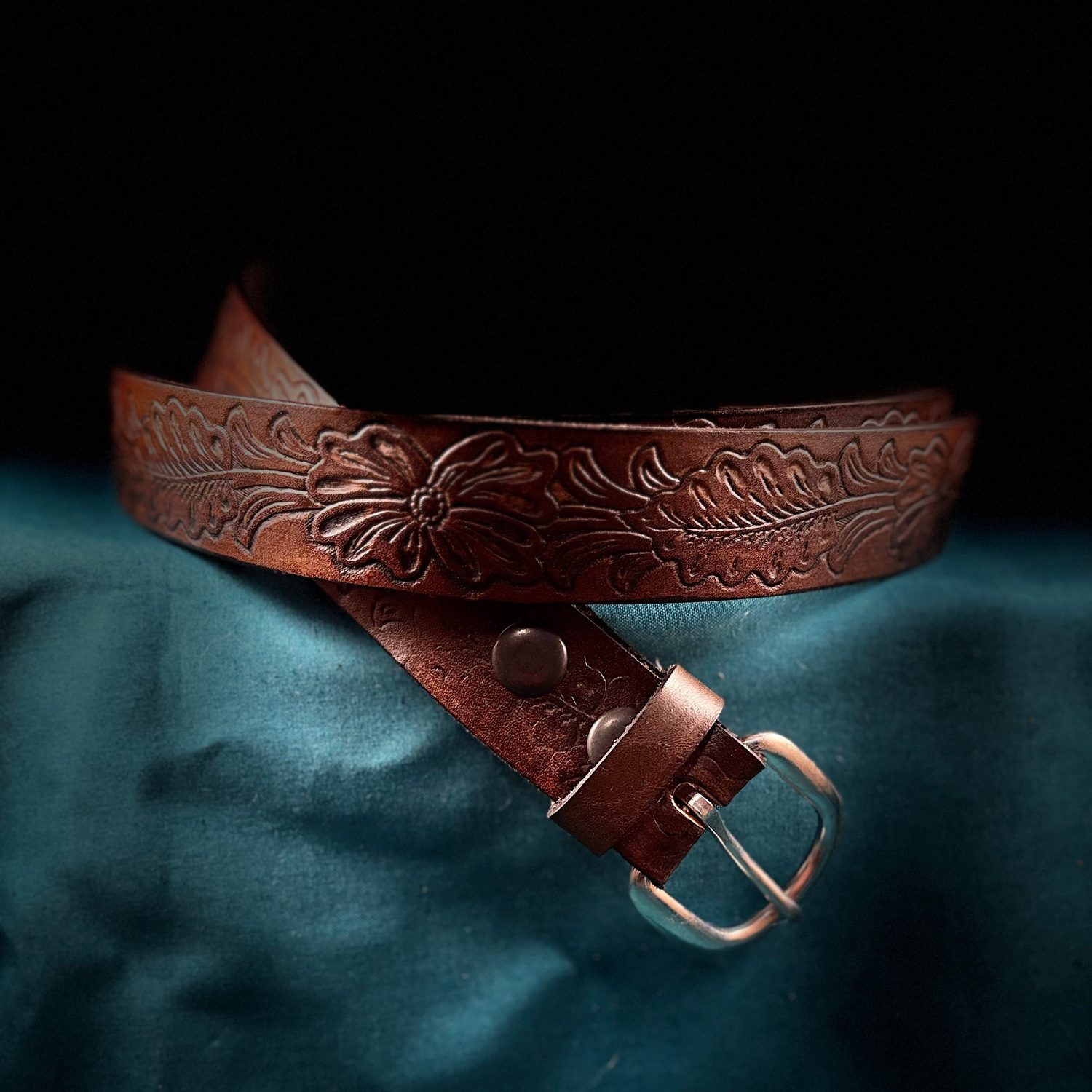 Brown leather belt with intricate designs on a teal fabric background