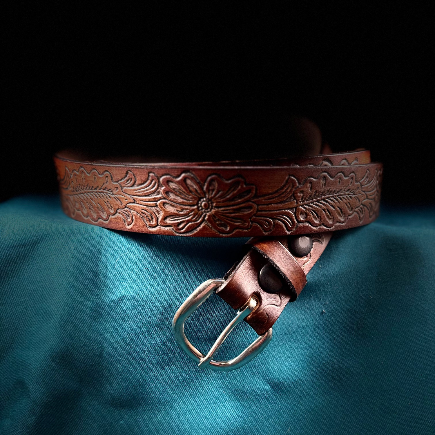 Brown leather belt with intricate designs on a blue fabric background