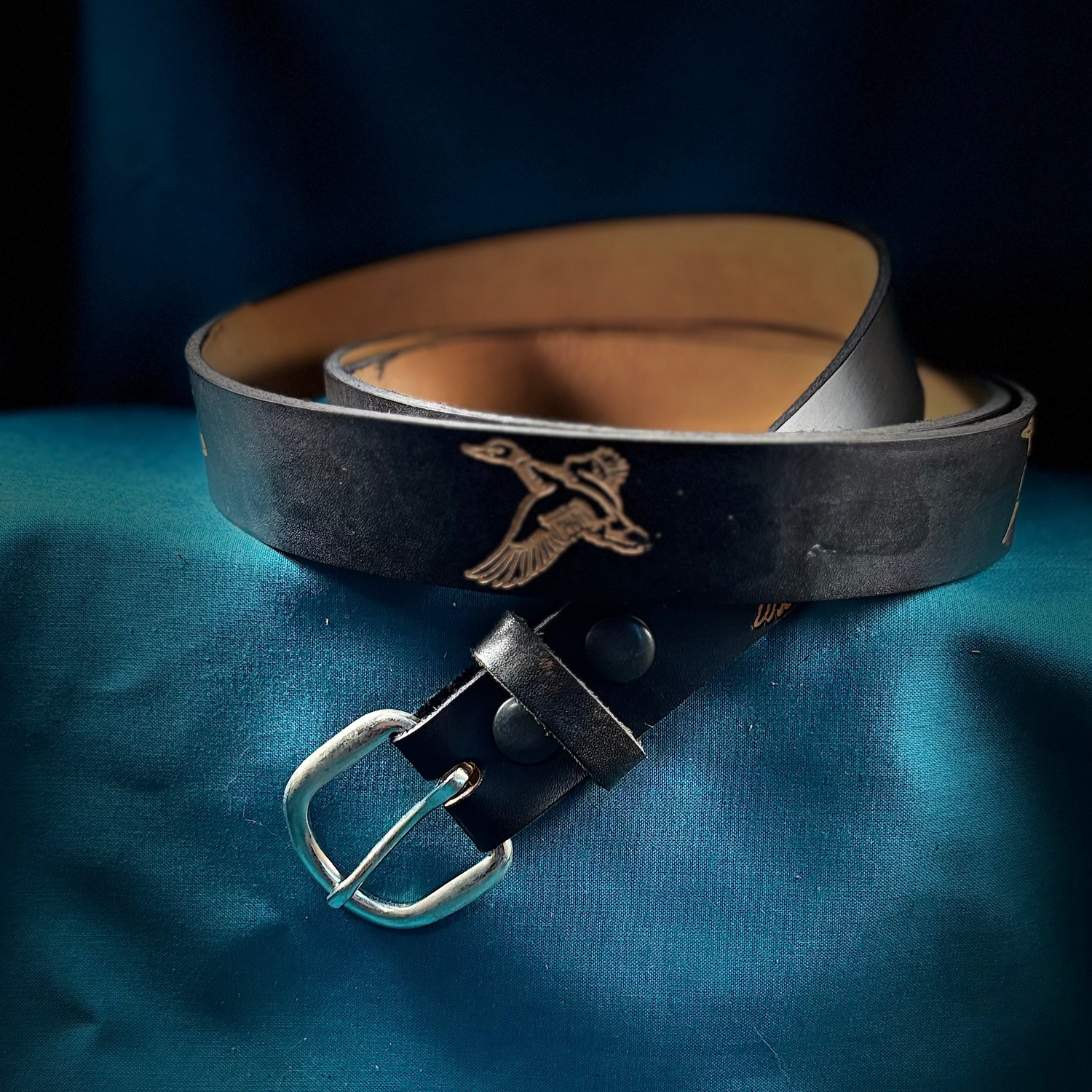 Black leather belt with silver buckle on a blue fabric background