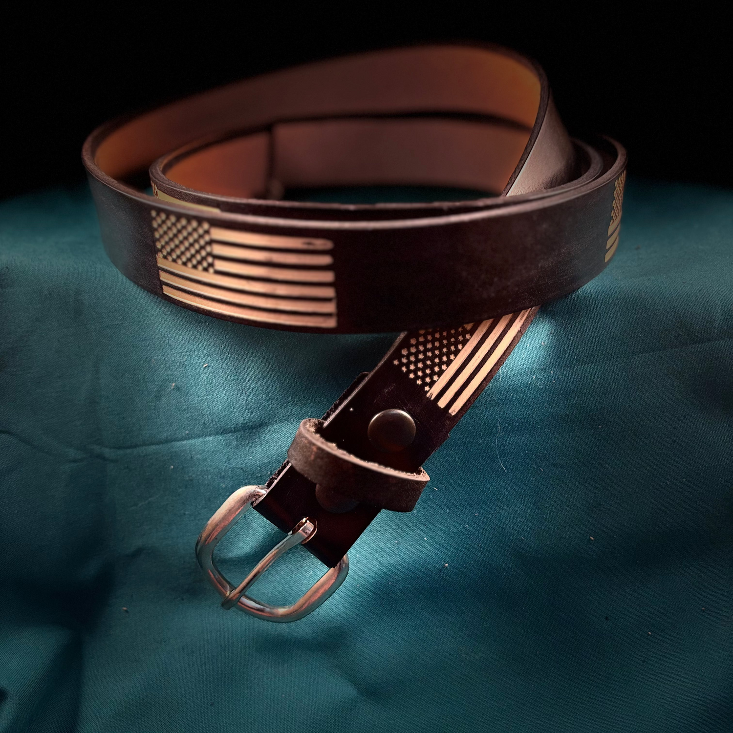 Brown leather belt with metallic buckle on a dark blue fabric background