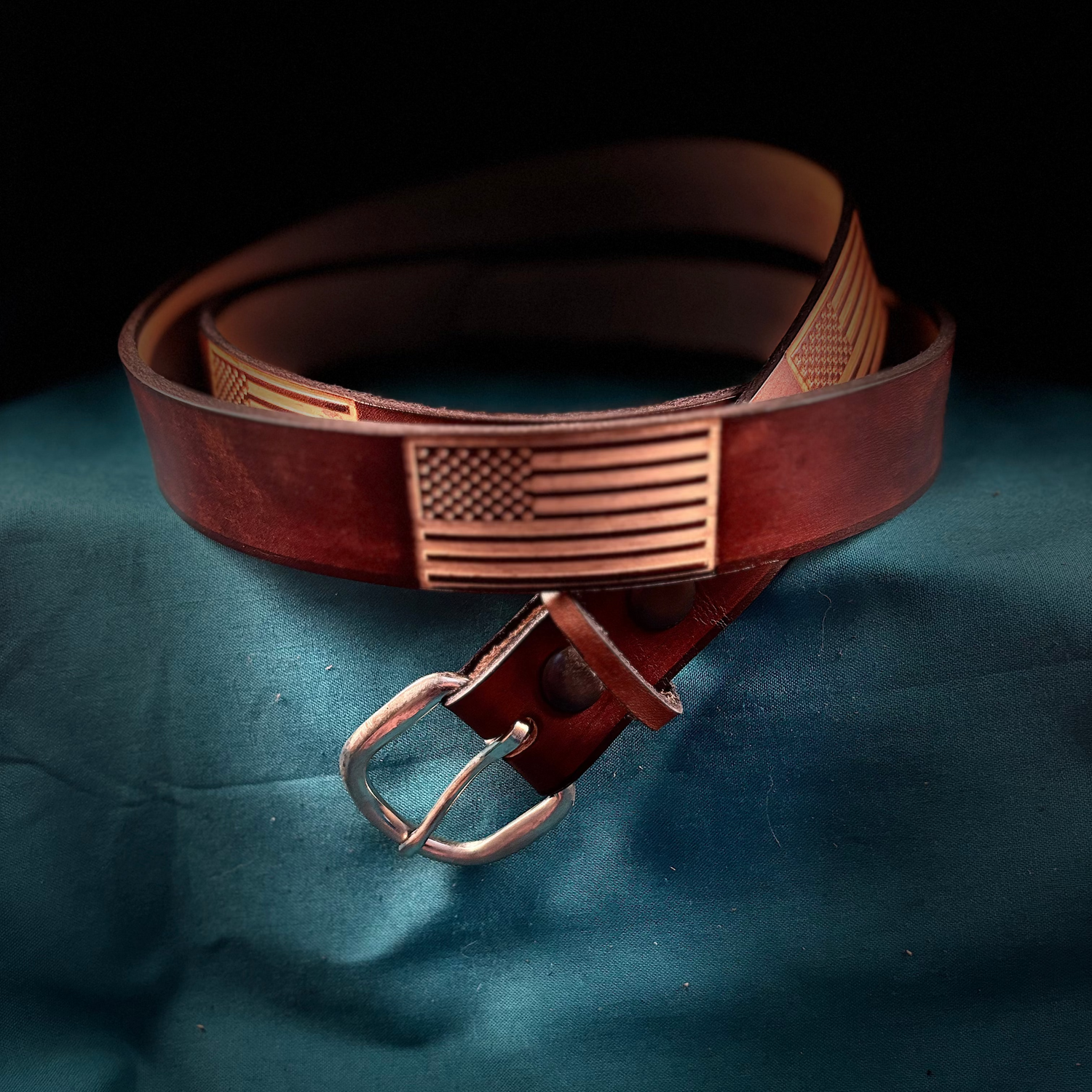 Brown leather belt with American flag buckle on a dark surface
