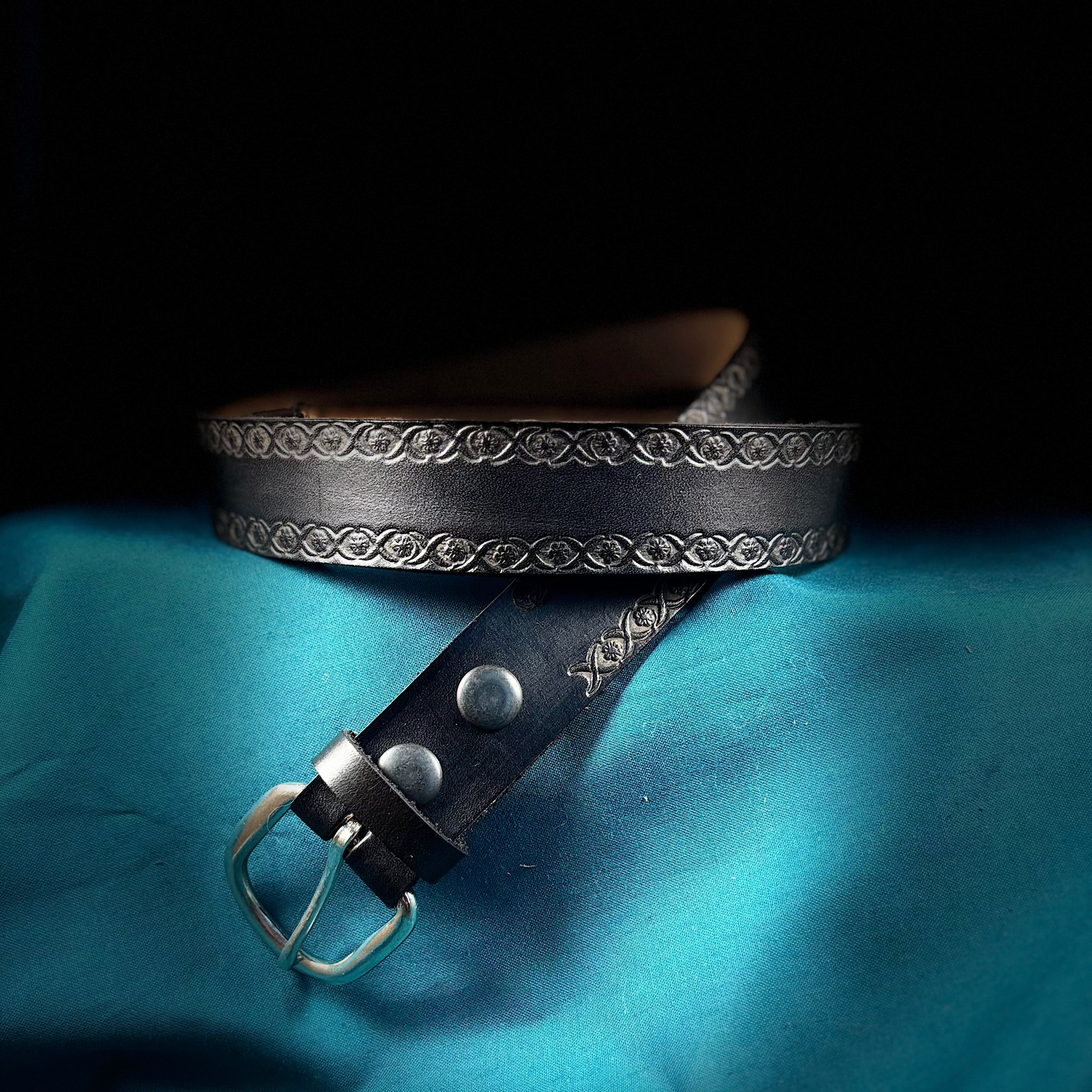 Black leather belt with silver buckle on a blue fabric background