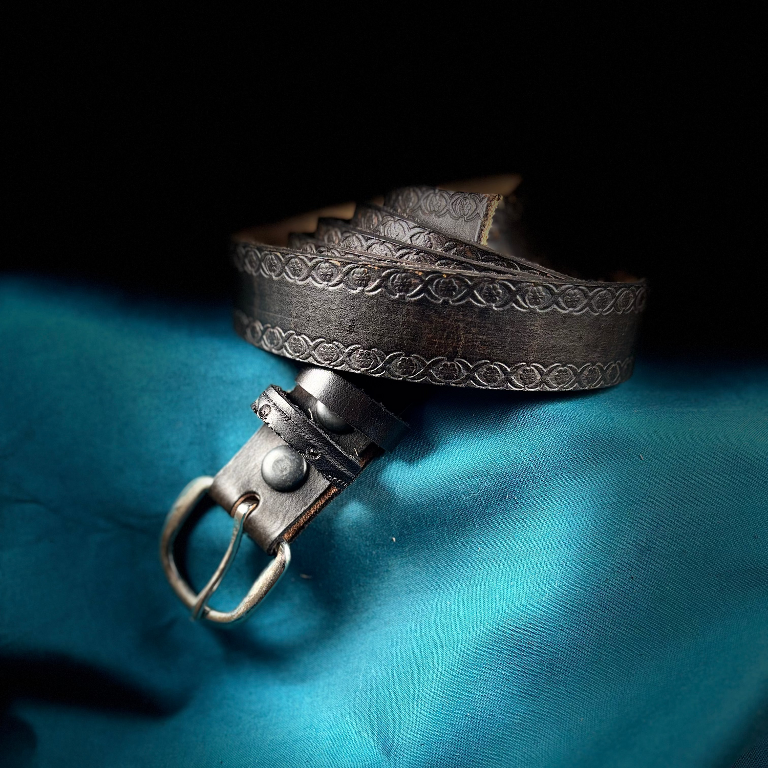 Brown leather belt with metal buckle on a blue fabric background