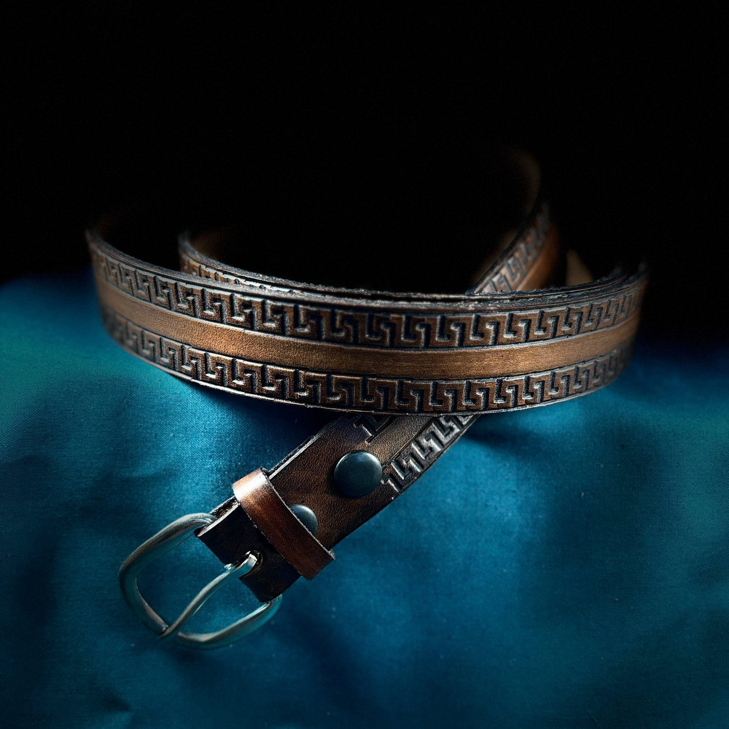 Brown leather belt with decorative pattern on a blue fabric background
