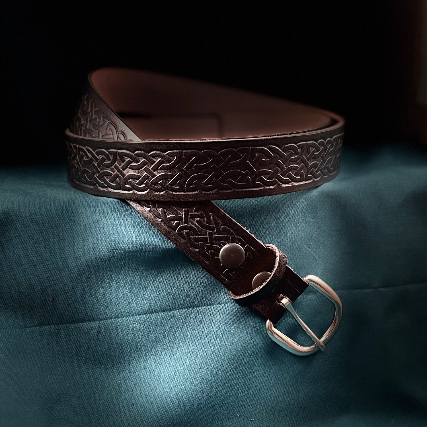 Brown leather belt with intricate design on a blue fabric background