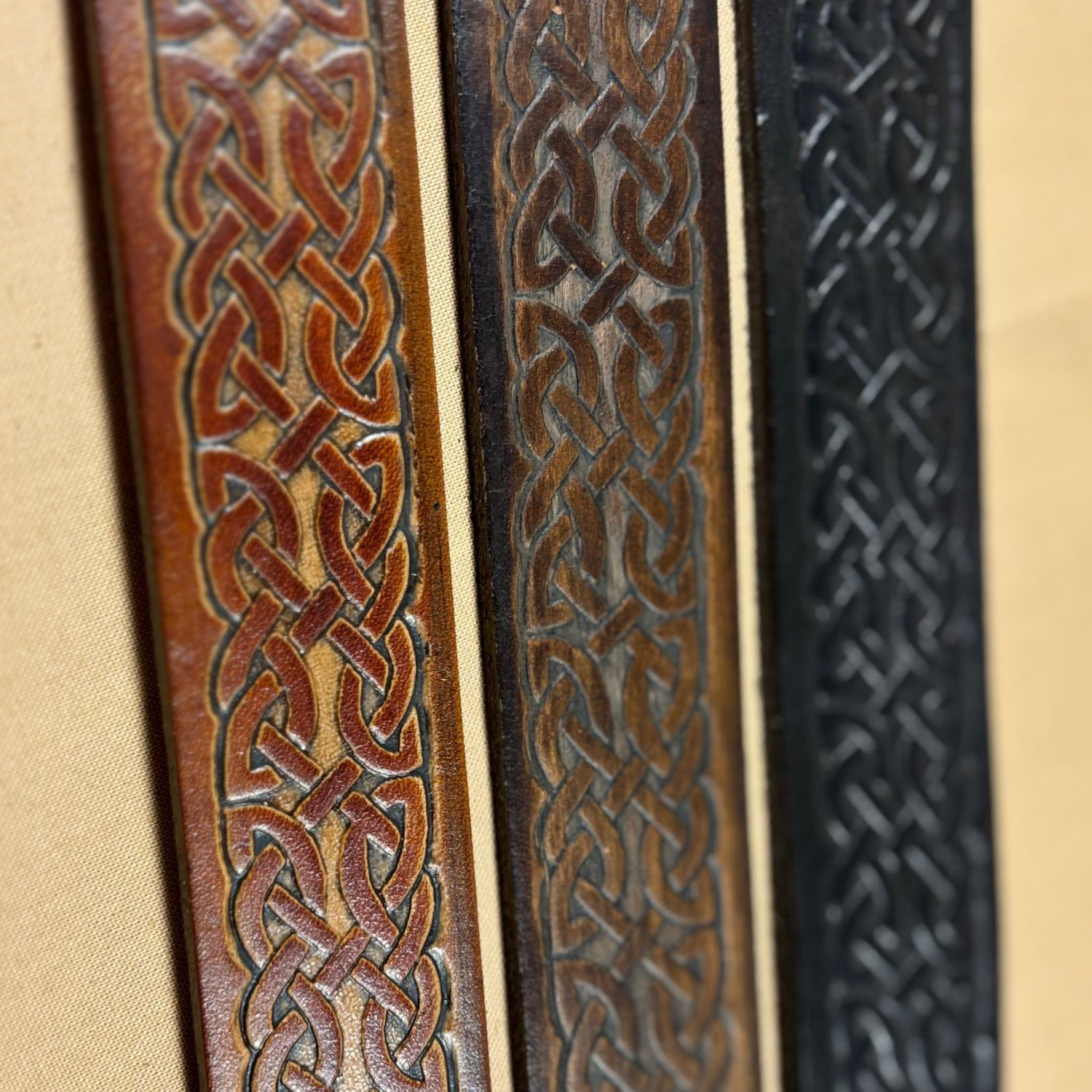 Three leather straps with intricate Celtic knot patterns on a beige background