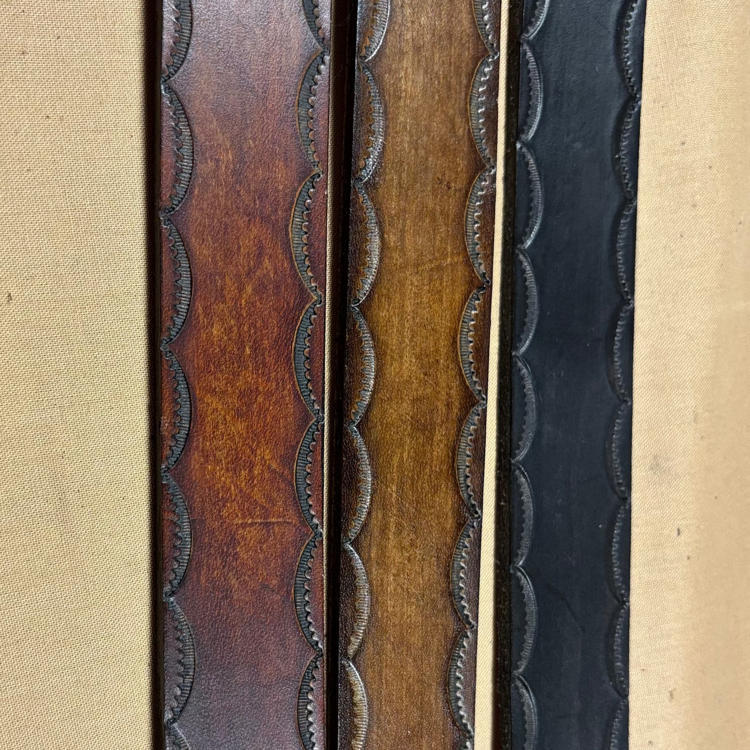 Three leather straps with different patterns and colors on a beige background