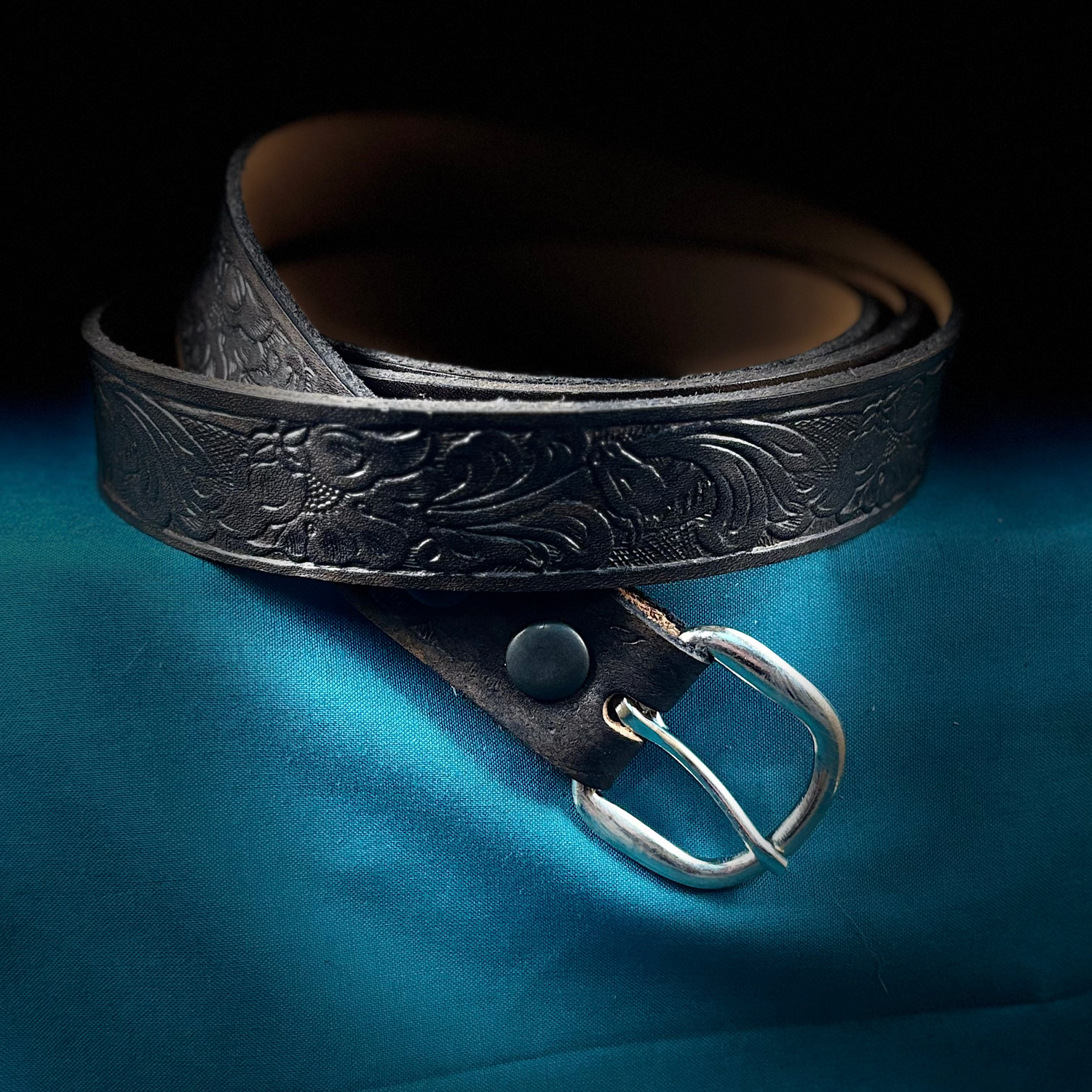 Black leather belt with silver buckle on a blue fabric background