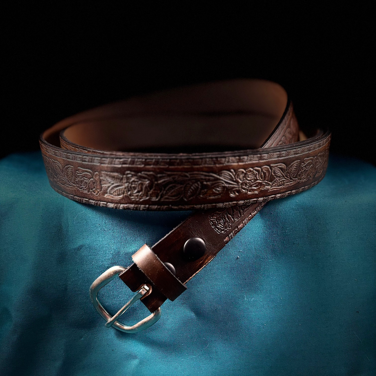 Brown leather belt with embossed design on a blue fabric background