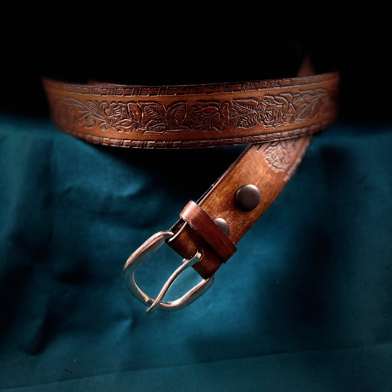 Brown leather belt with intricate designs on a dark blue fabric background
