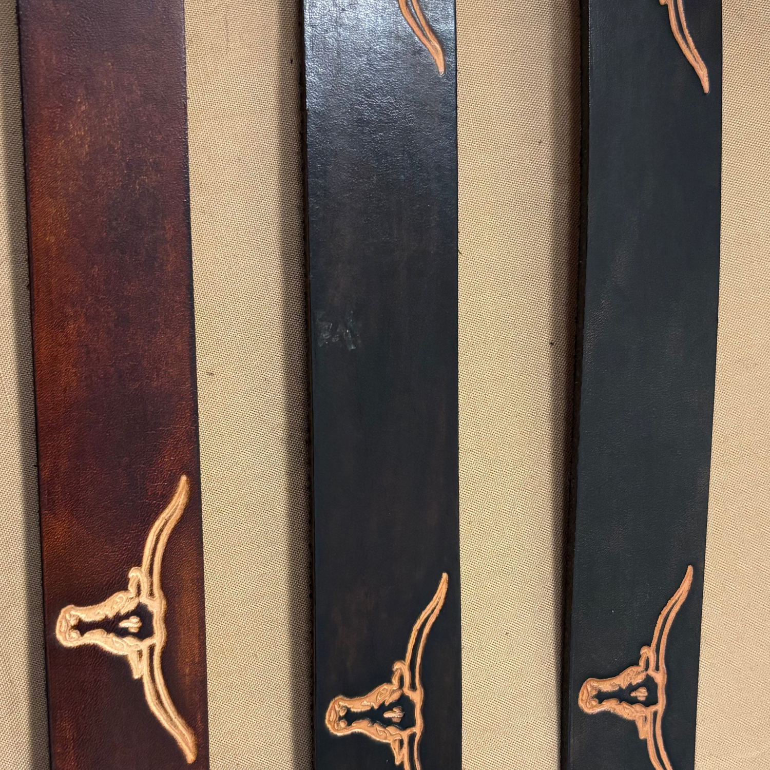 Three leather belts with a central brown belt flanked by two black belts on a beige background.