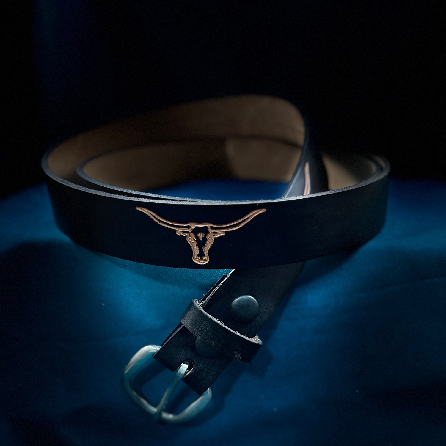 Black leather belt with a gold buckle on a blue surface