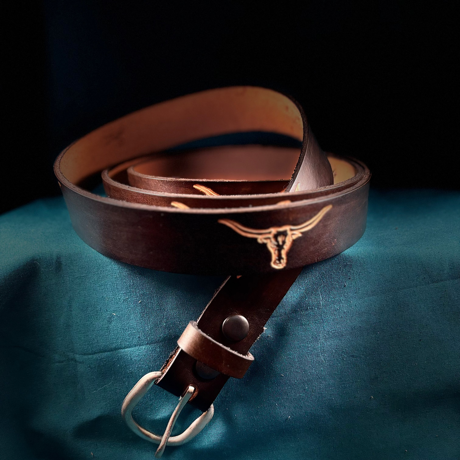 Brown leather belt with a metal buckle on a blue fabric background