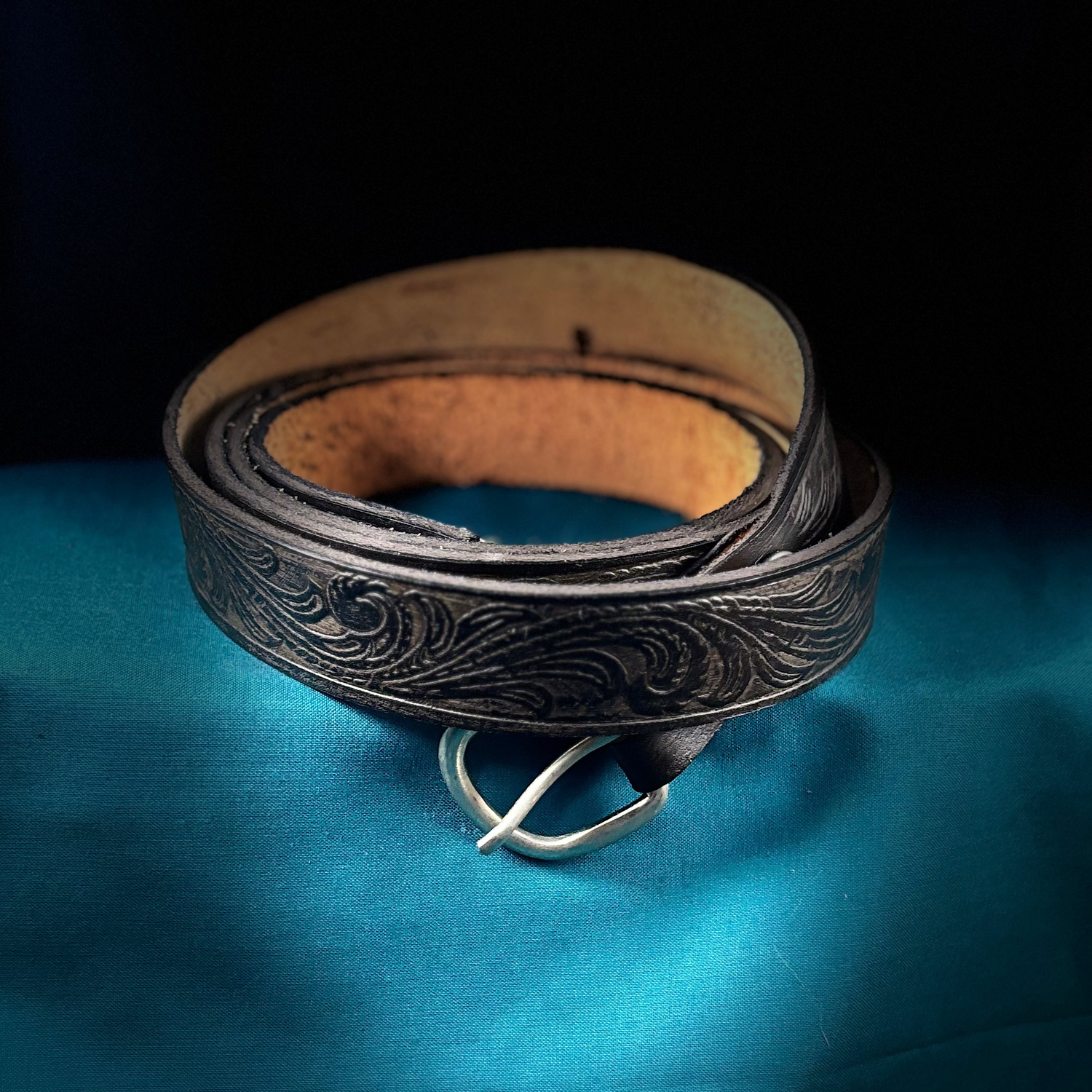 Black leather belt with intricate designs on a blue surface