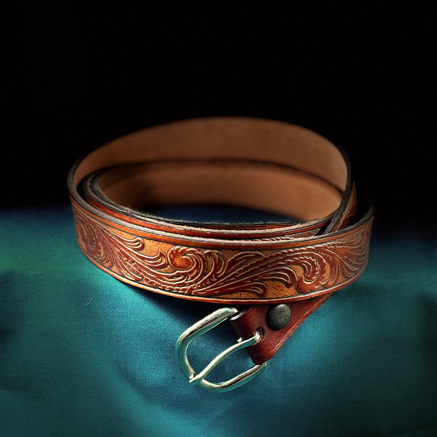 Brown leather belt with intricate designs on a green fabric background